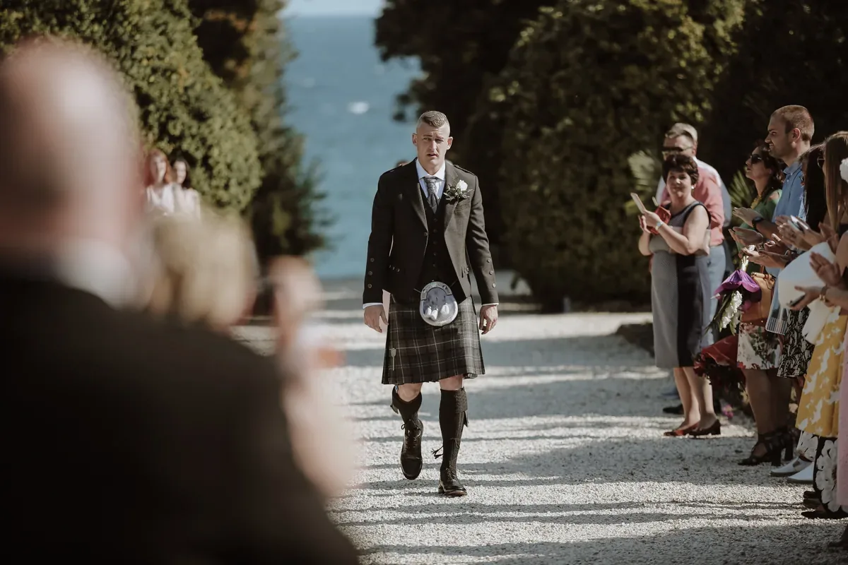 Bräutigam im Kilt beim Einzug, Gäste am Wegrand – dokumentarische Hochzeitsfotografie