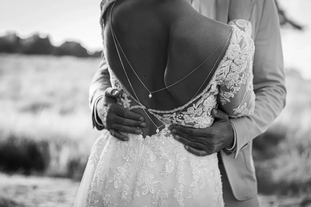 Umarmung des Brautpaars, Spitzenkleid mit Rückenkette – Schwarzweiß-Detail